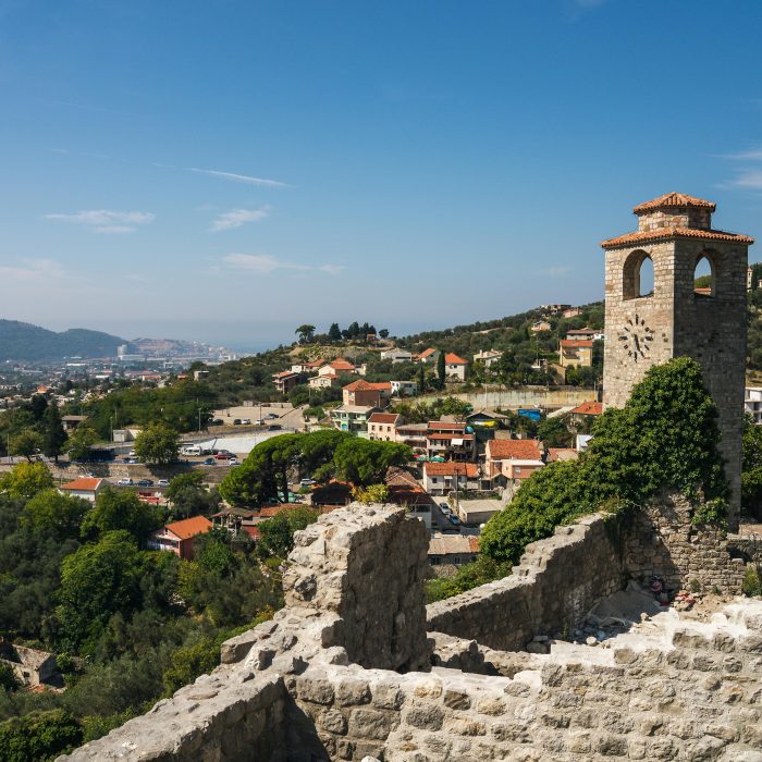 Explore the historic landscape of an old town featuring ancient ruins and a prominent tower under a sunny sky.